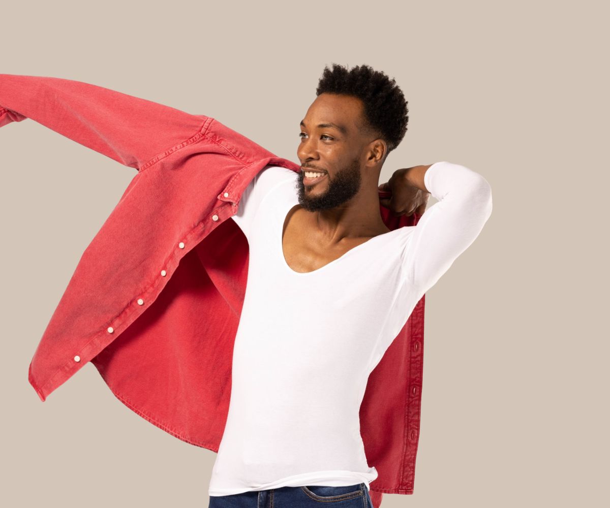 Man putting on red shirt over his white undershirt for men