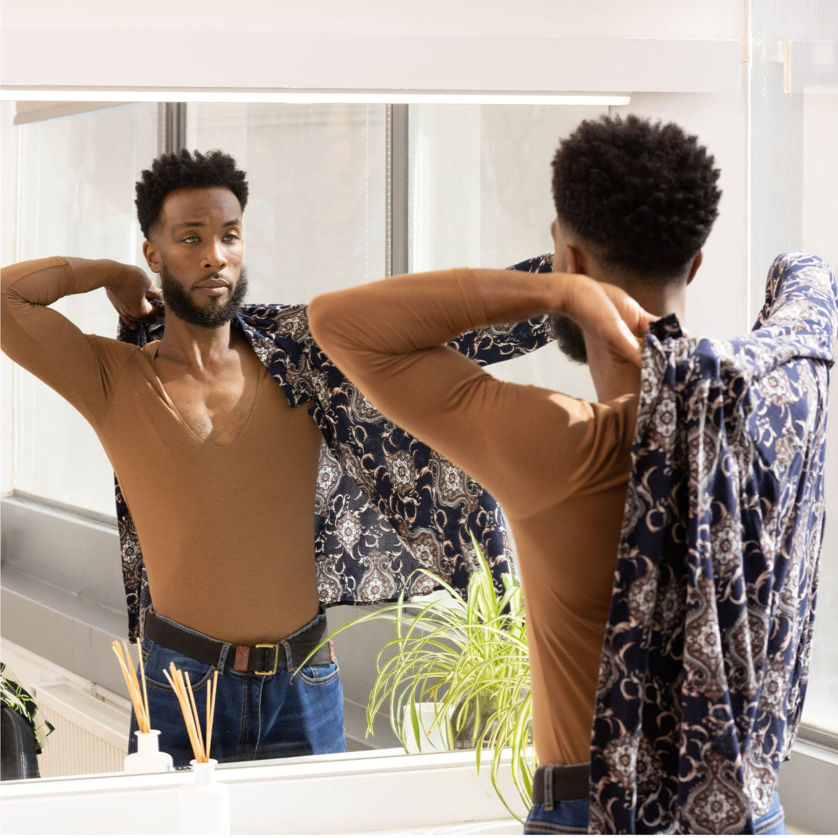 Man getting changed in the mirror putting his shirt on over his invisible undershirt